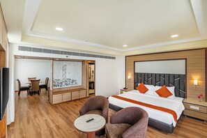 A hotel room with a bed, two armchairs, a small table, a desk with chairs, and a decorative wall panel.