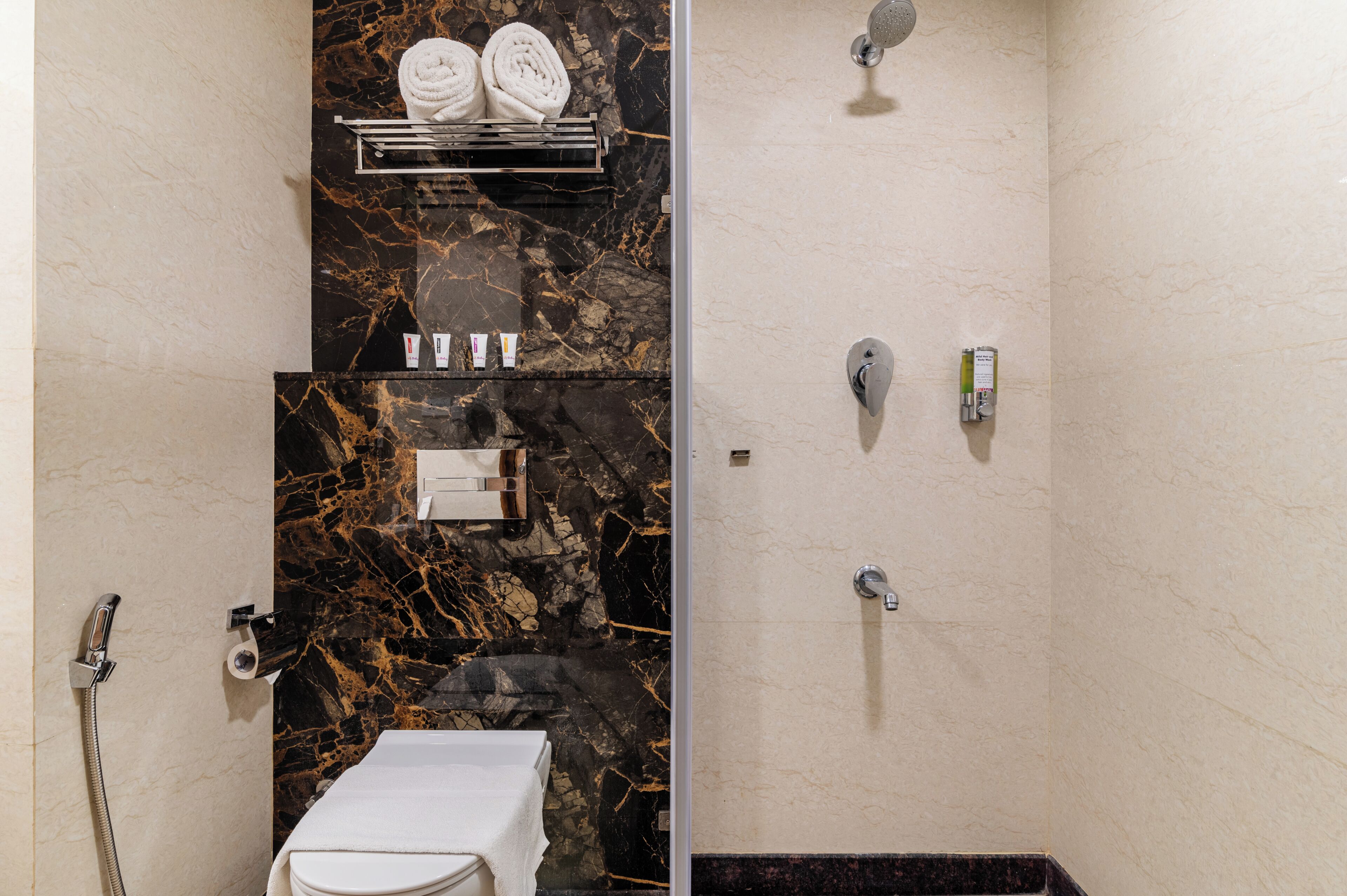 A bathroom with a marble wall, a towel rack with towels, a toilet, a shower area, and a sink.