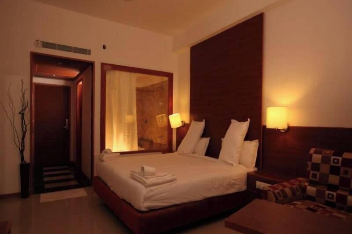 A hotel room with a bed, bedside lamps, a mirror, a sofa, and a small table.