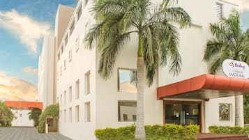 Experience the elegant Sterling Grand Madurai, a beautifully designed hotel with a symmetrical facade and lush palm trees.