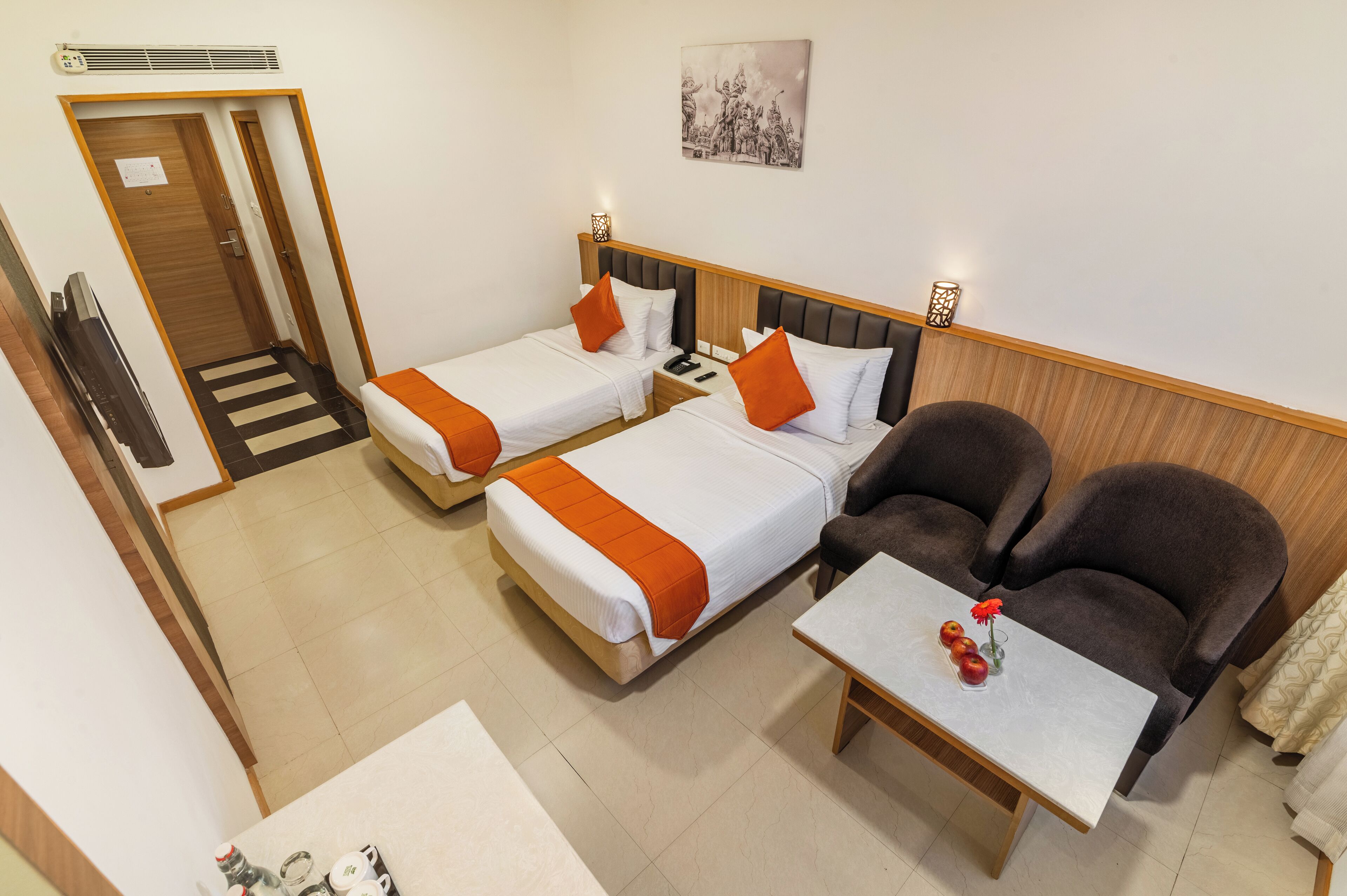 Habitación de hotel con dos camas, un sofá, una mesa con un florero y un televisor.
