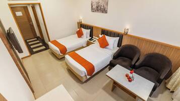 A hotel room with two beds, a sofa, a table with a vase, and a television.