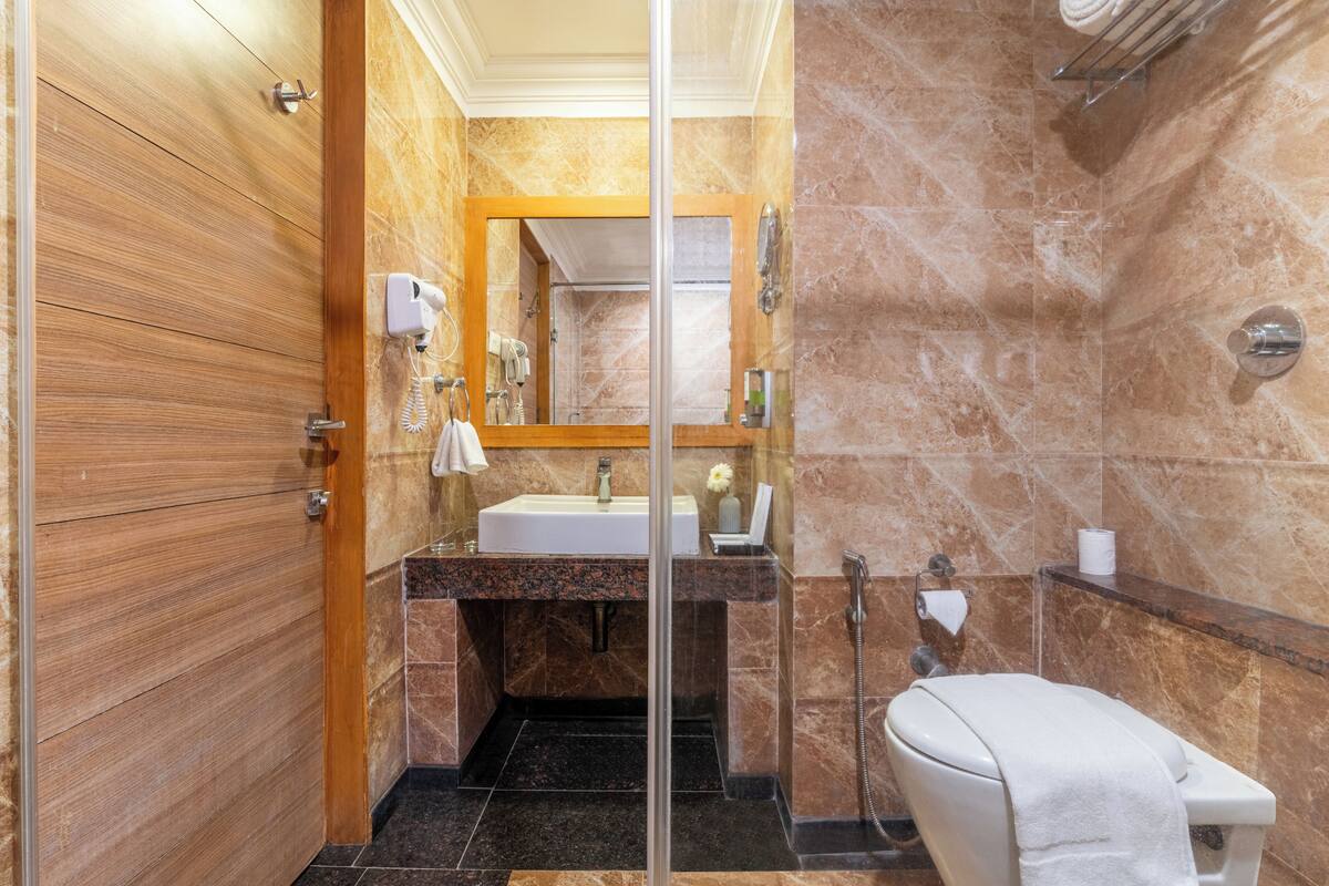 A bathroom with a wooden door, a sink with a mirror, a toilet, and a shower area.