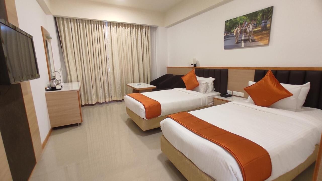 A hotel room with two beds, a desk, a chair, a TV, and a window with curtains.