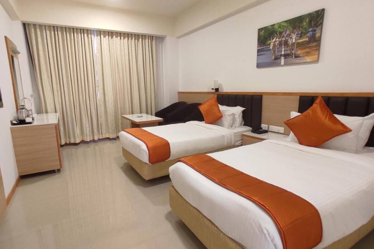 A hotel room with two beds, a desk, a chair, a TV, and a window with curtains.