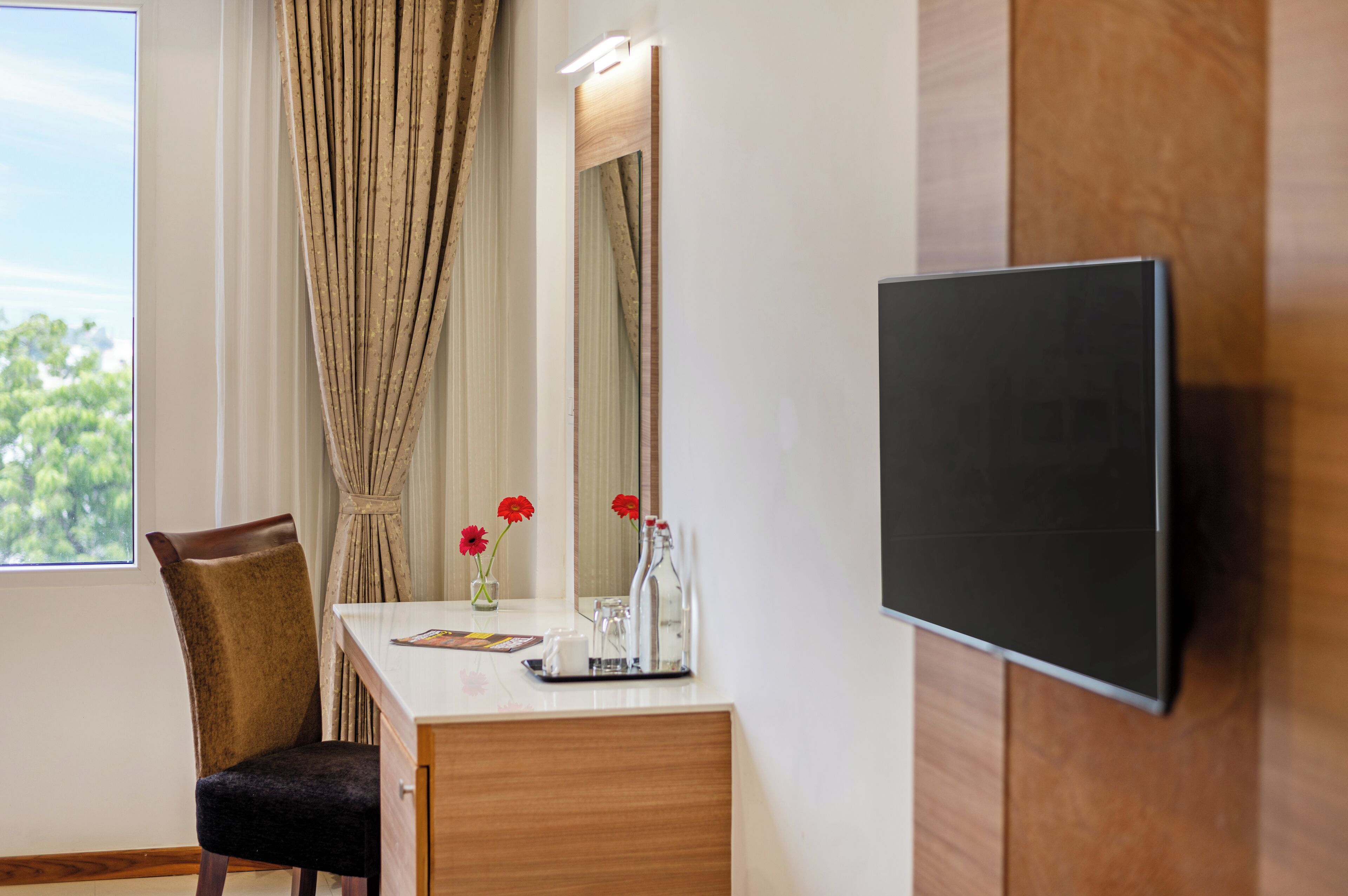 Ein Hotelzimmer mit Holzschreibtisch, einem Sessel, einem Flachbildfernseher, einem Spiegel und einem Fenster mit Vorhängen.