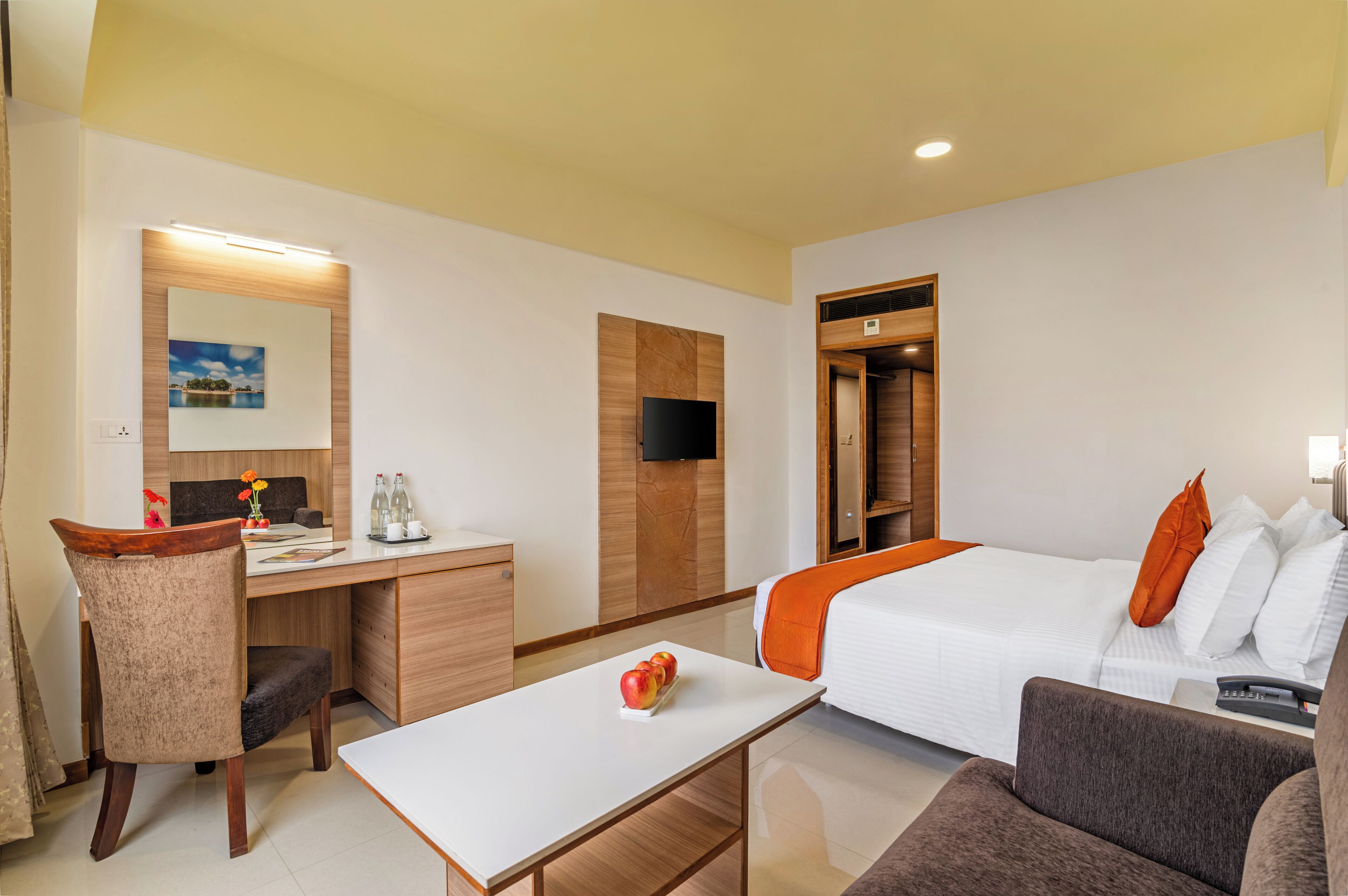 A hotel room with a bed, a desk, a chair, a small table, and a TV.