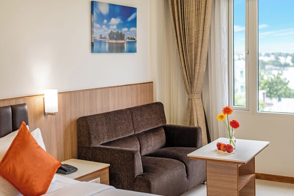 A hotel room with a bed, a brown sofa, a small table with flowers, a nightstand, and a painting on the wall.