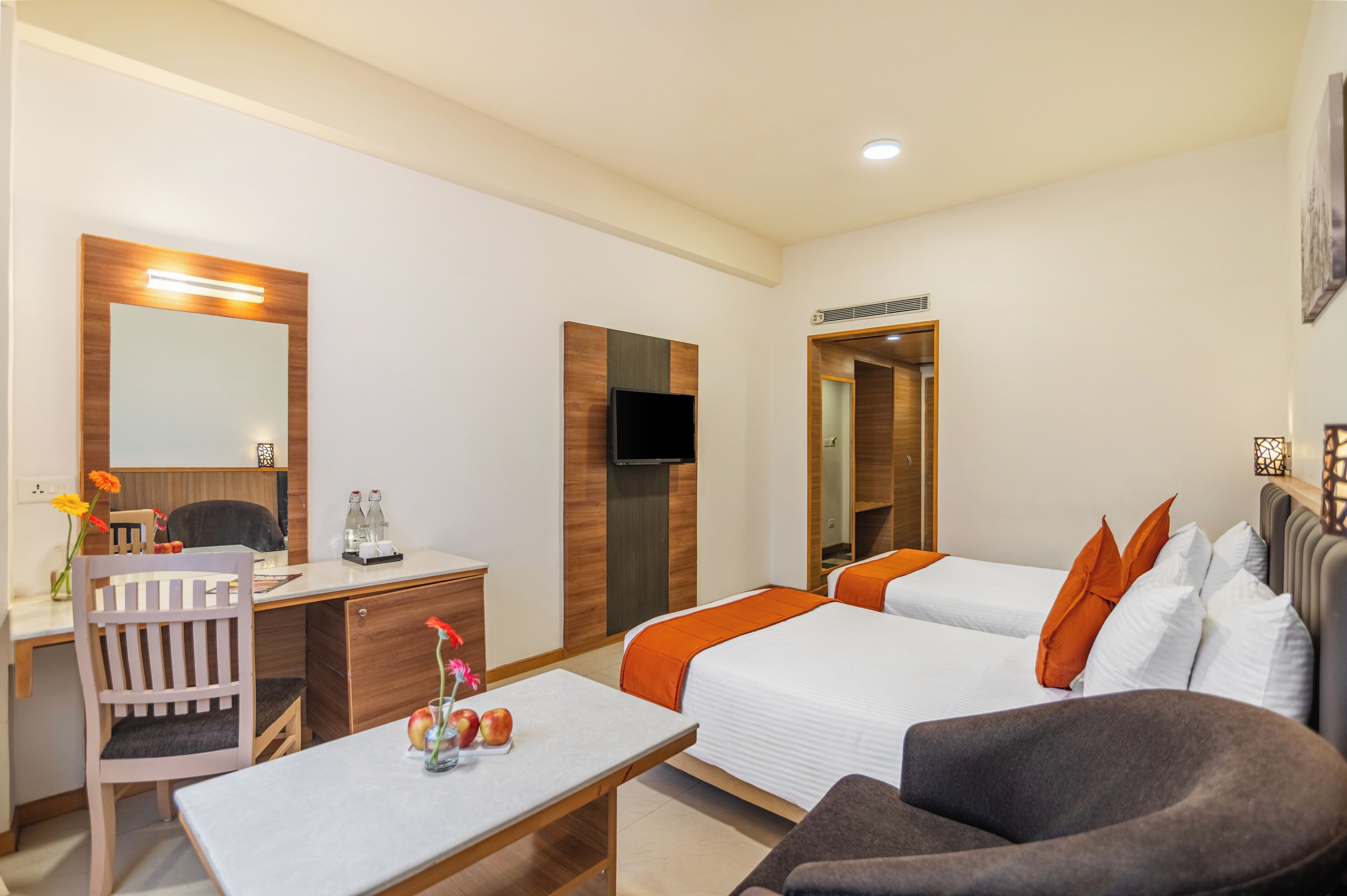 Quarto de hotel com escrivaninha, duas camas, televisão e espelho.
