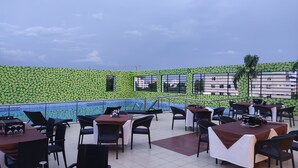 An outdoor dining area with tables and chairs, a pool, and a green leafy wall. - Sterling V Grand Madurai (Madurai)