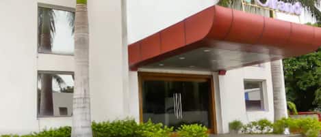 A hotel entrance with a red awning, palm trees, and a sign that reads "V Grand".