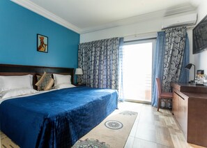 A hotel room with a large bed, a desk, a chair, a TV, and a window with curtains. - Residences Feto II (Dakar)