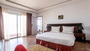 Un dormitorio con una cama grande, una mesita de noche, una lámpara, una silla roja y vistas al exterior a través de una puerta corrediza.