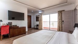 Habitación de hotel con una cama grande, un escritorio con una silla roja, un televisor de pantalla plana y un balcón con cortinas.