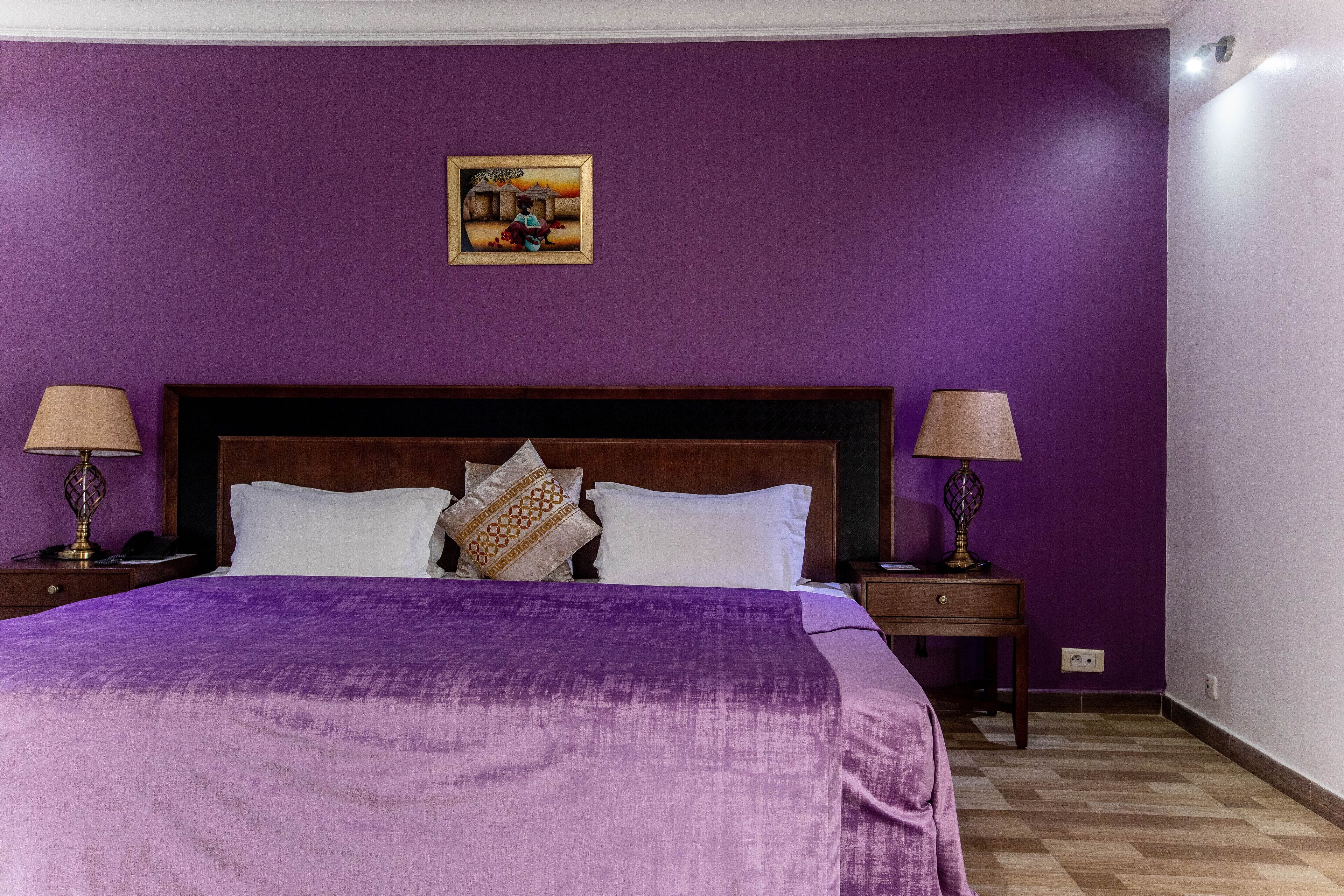 A bedroom with purple walls, a wooden headboard, white bedding, and two bedside lamps.