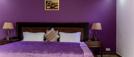 A bedroom with purple walls, a wooden headboard, white bedding, and two bedside lamps.
