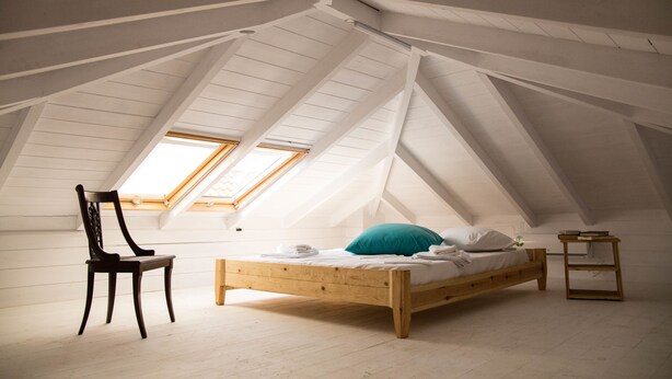 Dormitorio abuhardinado con techos altos, una cama de madera, una silla y una mesita de noche pequeña.