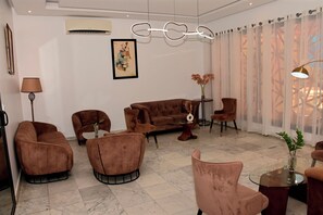 A modern living room with a brown sofa, armchairs, a glass coffee table, and a lamp. - Résidence Feto III (Dakar)