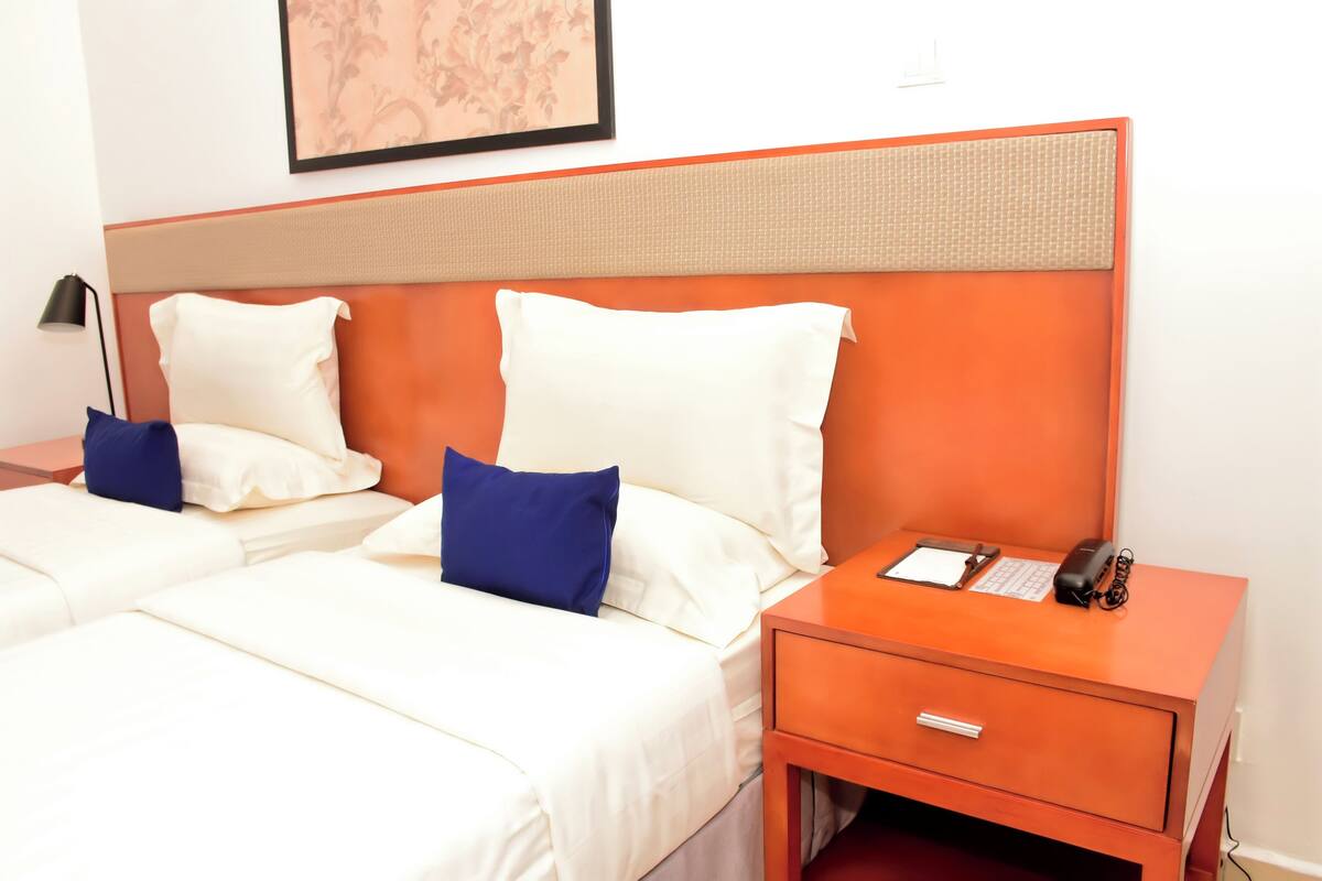 A hotel room with two beds, a nightstand with a phone and a lamp, and a framed picture on the wall.
