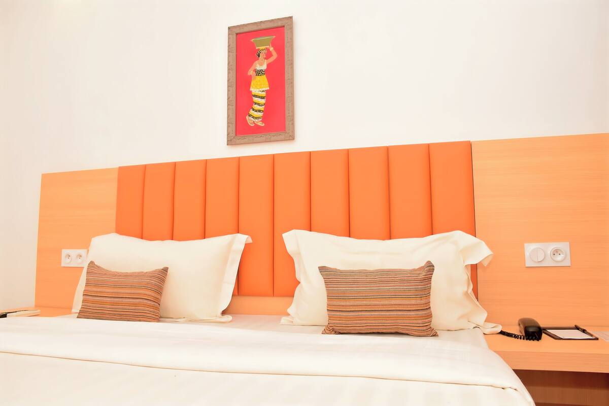 A hotel room with a bed, pillows, a nightstand, a phone, and a wall-mounted picture.