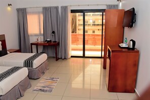 A hotel room with two beds, a desk, a chair, a TV, a balcony, and a sliding door. - Résidence Feto III (Dakar)