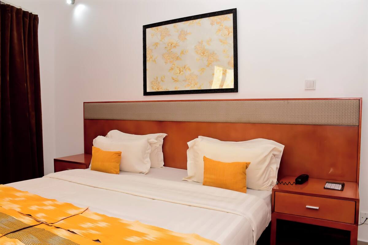 A hotel room with a bed, a nightstand, a framed picture on the wall, and a brown curtain.