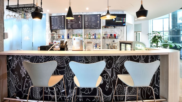 Un espace bar moderne avec trois chaises, un comptoir et un éclairage suspendu au plafond.