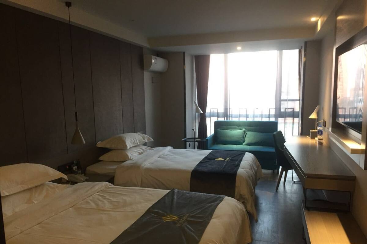 A hotel room with two beds, a sofa, a desk, and a large window with a view.