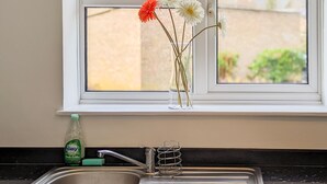 A kitchen sink with a faucet and a glass vase with flowers on the window sill. - Outfield Homes (Peterborough)