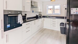 A modern kitchen with white cabinets, a black countertop, and a stainless steel refrigerator. - Outfield Homes (Peterborough)