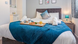 A neatly made bed with a blue blanket, a tray with croissant, orange juice, and a cup, and towels on the side. - Outfield Homes (Peterborough)