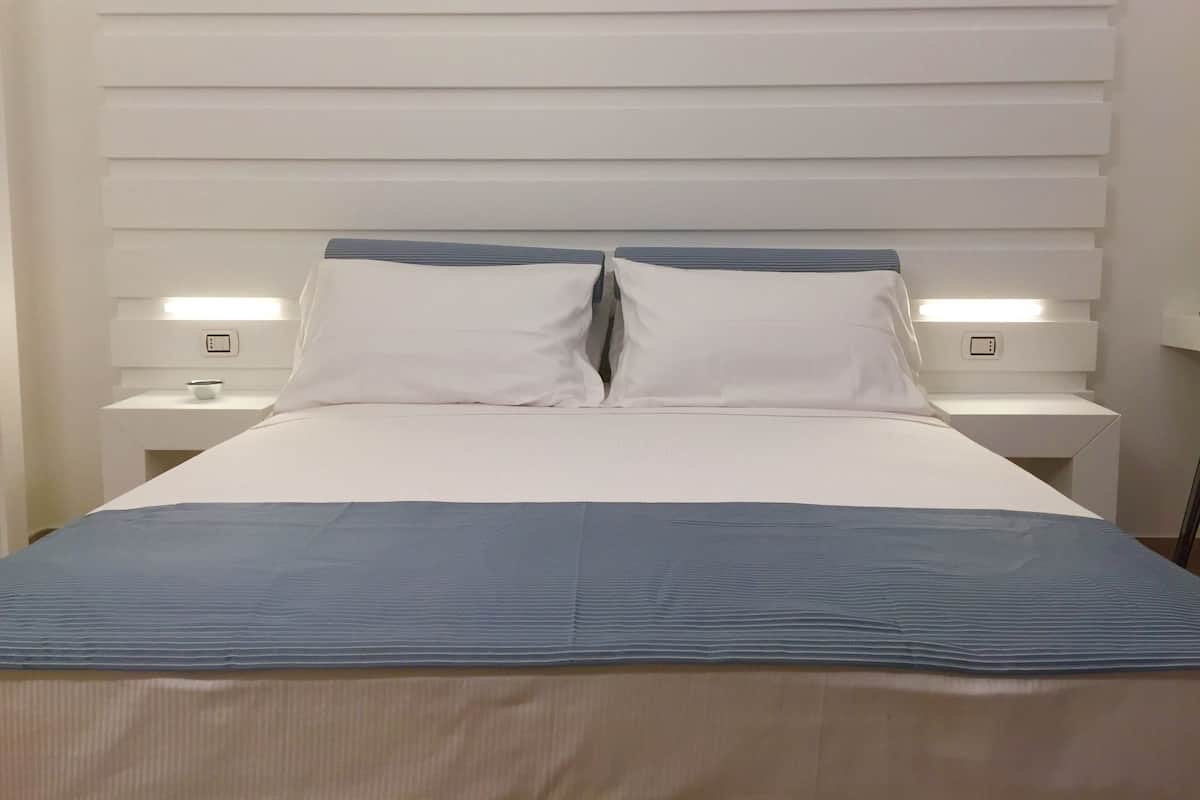 A modern hotel room with a large bed, white headboard, and bedside lamps.