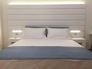 Una habitación de hotel moderna con una cama grande, cabecera blanca y lámparas de noche.