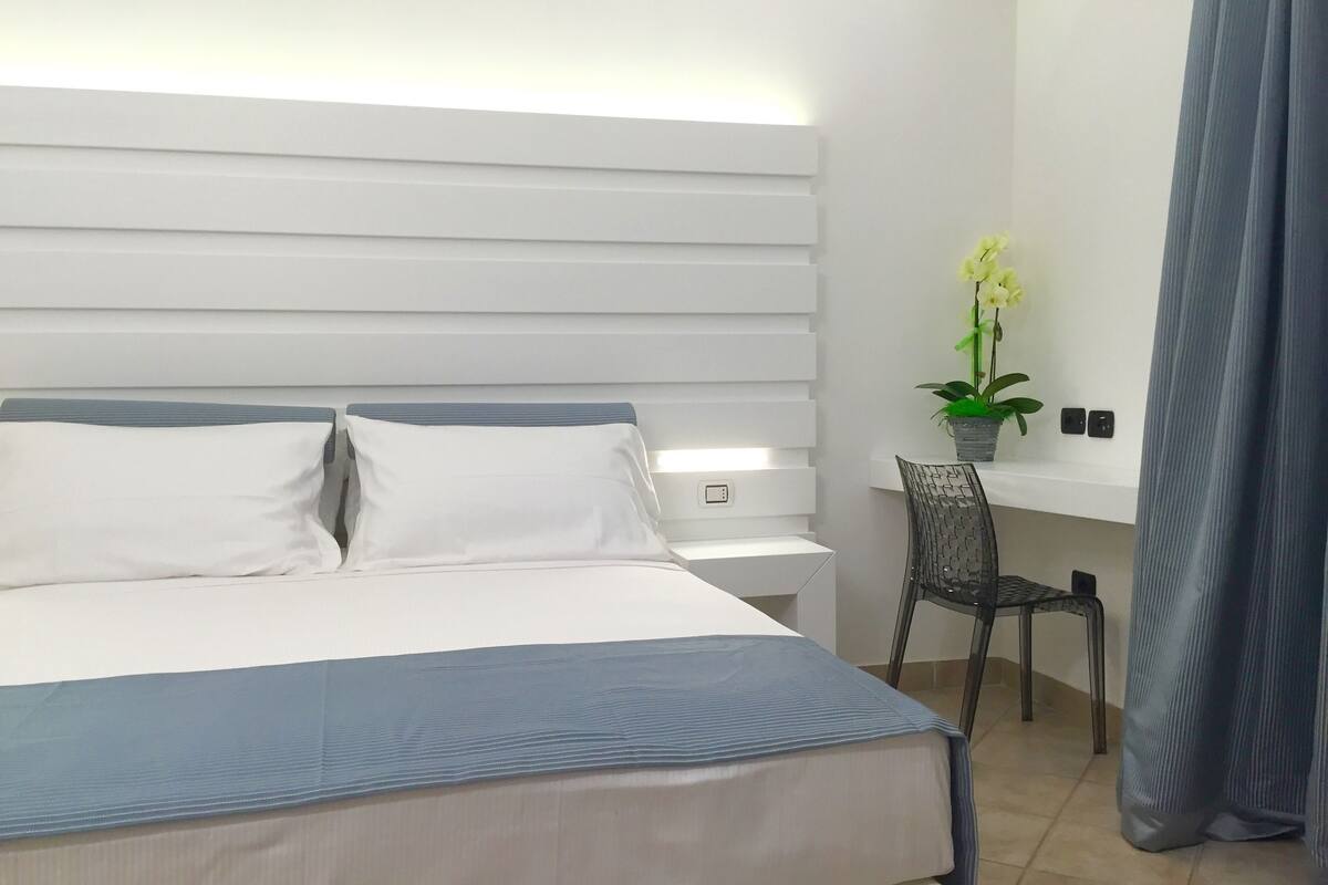 A modern hotel room with a large bed, a desk, and a chair.