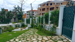 Un sendero pavimentado que conduce a una entrada porticada, rodeada de vegetación y edificios residenciales.