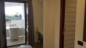 Una habitación con balcón, cama, silla y escritorio.
