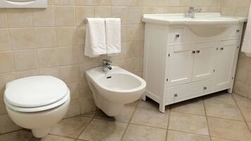 Une salle de bain comprenant des toilettes, un bidet et un meuble-lavabo blanc avec un évier.