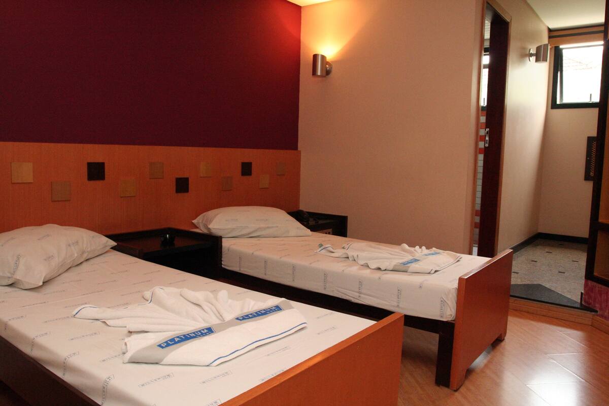 Ein Hotelzimmer mit zwei Einzelbetten, einem Holzkopfteil, einer roten Akzentwand und einem kleinen Fenster.