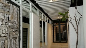 Un pasillo con paredes de ladrillo blanco, vigas de madera y un sillón tapizado en gris.
