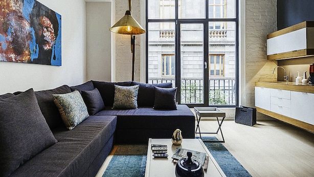 Una sala de estar moderna con un sofá oscuro, una mesa de centro y un ventanal con vistas a edificios.