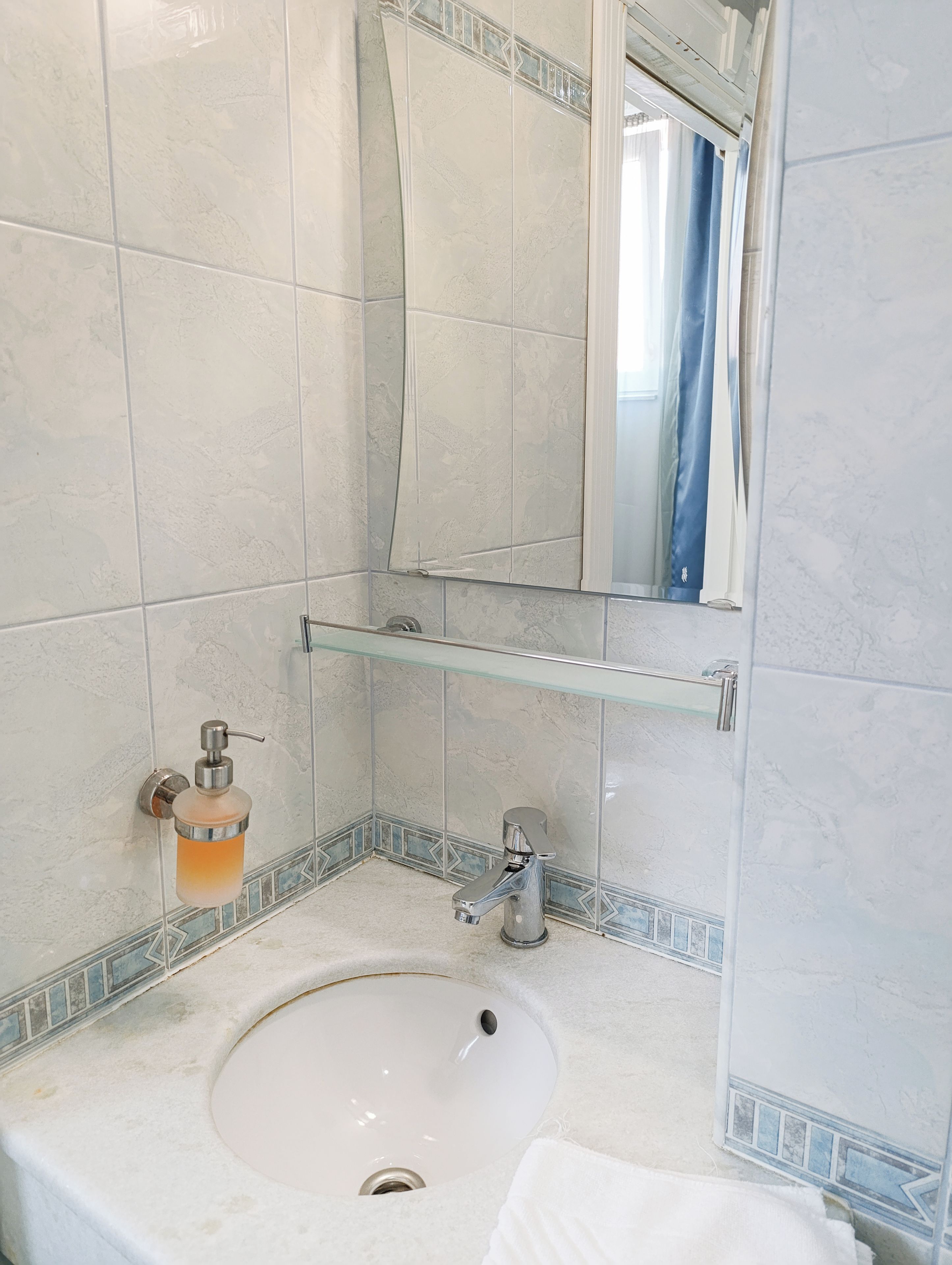 Un baño con lavamanos blanco, espejo y dispensador de jabón de vidrio.