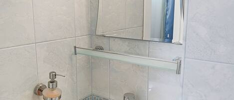 Un baño con lavamanos blanco, espejo y dispensador de jabón de vidrio.