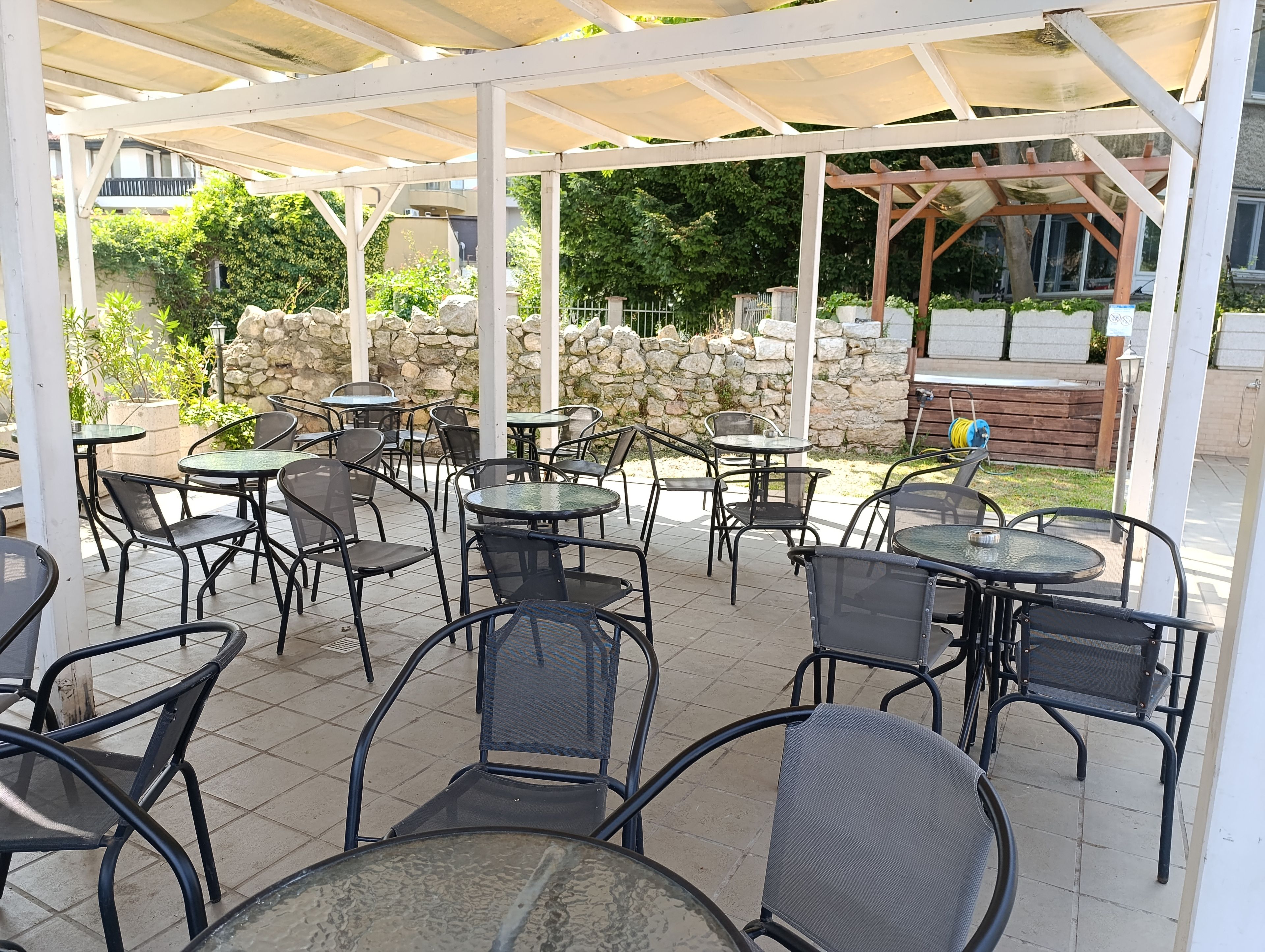 An outdoor patio area with multiple tables and chairs, a stone wall, and a covered seating area.