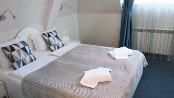 Habitación de hotel con cama, almohadas, manta, mesita de noche y ventana con cortinas.