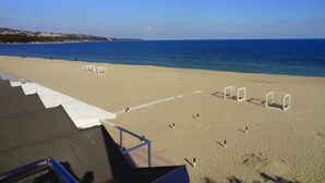 Una playa con cielo despejado, orilla arenosa y estructuras blancas que parecen parte de una cancha de voleibol de playa.