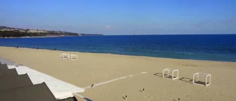 Una playa con cielo despejado, orilla arenosa y estructuras blancas que parecen parte de una cancha de voleibol de playa.