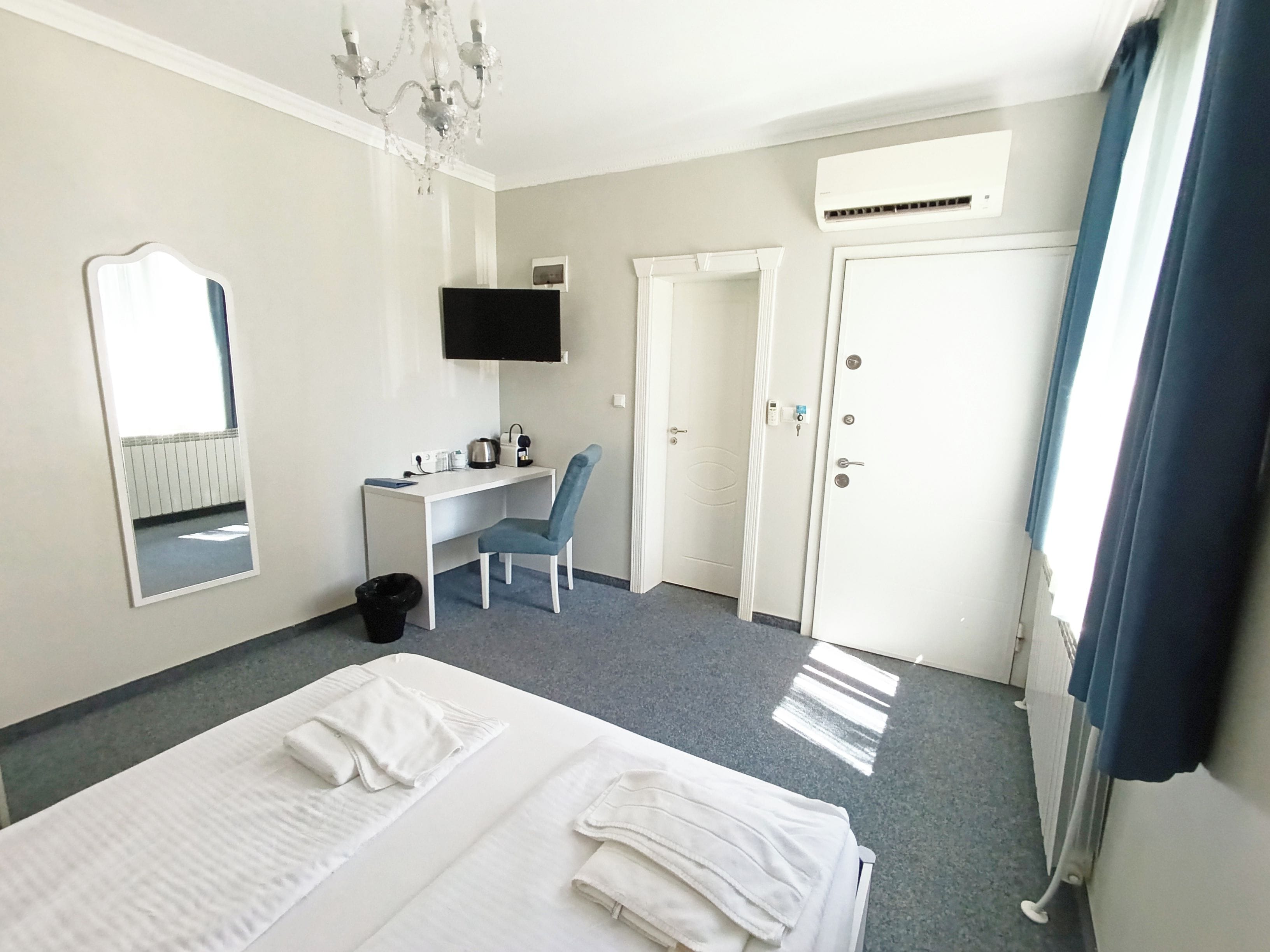 A hotel room with a bed, a desk, a chair, a TV, and a door.