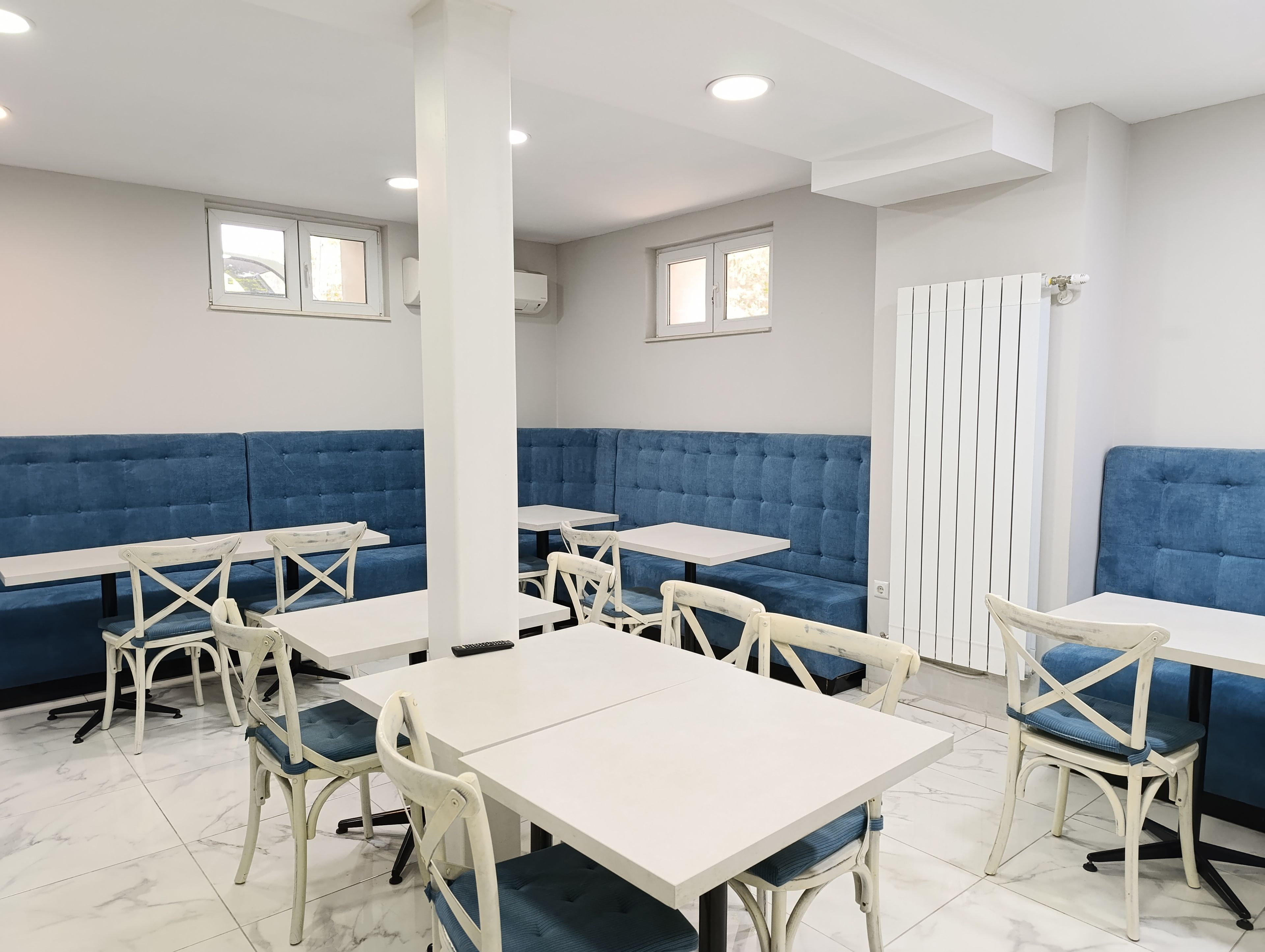 A restaurant interior with blue cushioned booths, white tables, and chairs.
