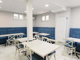Interior de restaurante con asientos acolchados azules, mesas y sillas blancas.