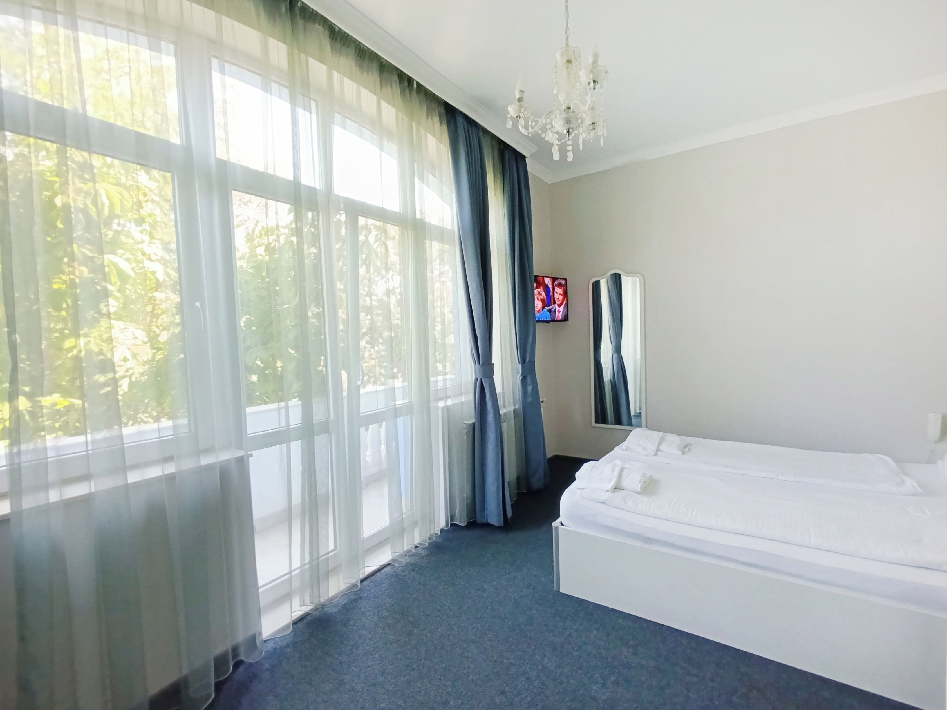 A hotel room with a bed, a television, and a window with sheer curtains.